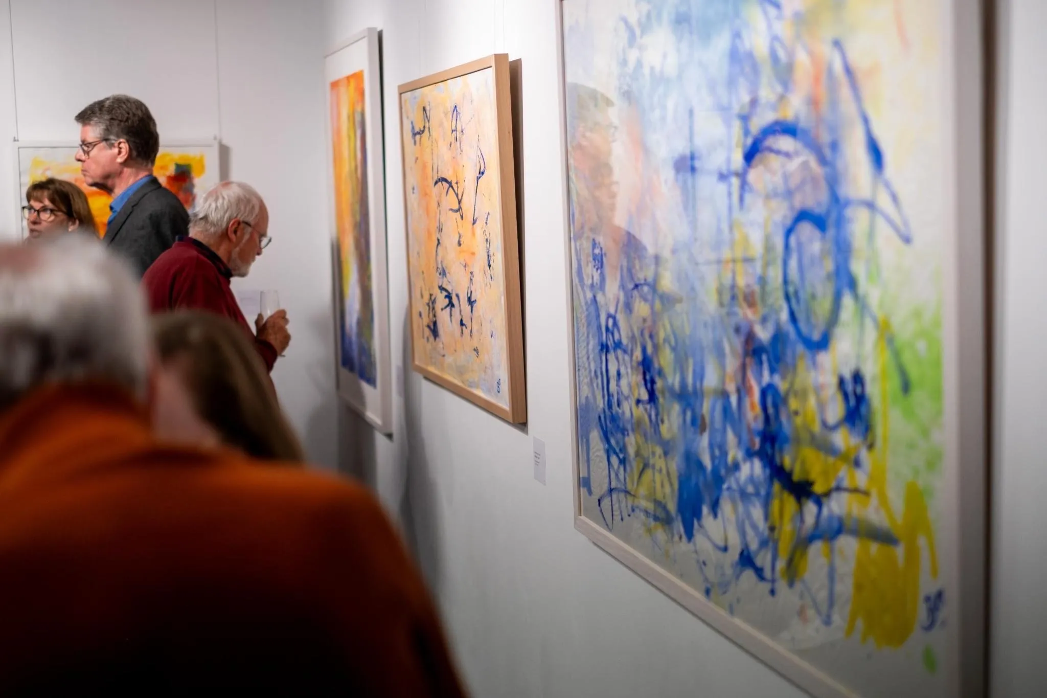 Visitors viewing paintings along the gallery wall